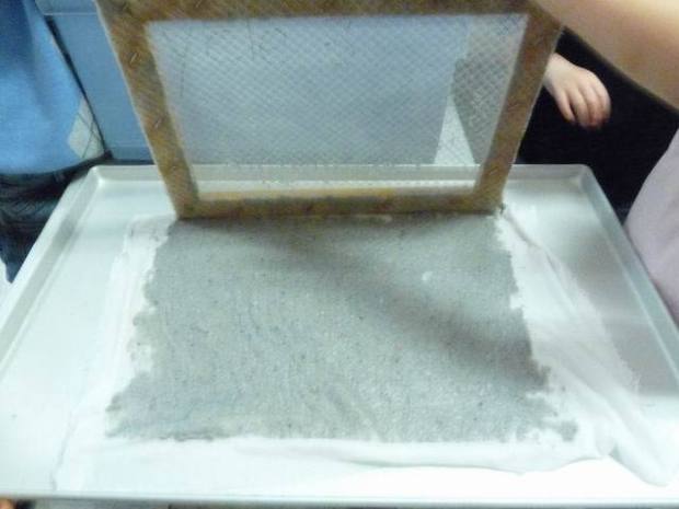 On retourne le tamis avec le tissu et on enlève délicatement le tamis. La pâte à papier reste collée sur le tissu. On retourne le tamis avec le tissu et on enlève délicatement le tamis. La pâte à papier reste collée sur le tissu.